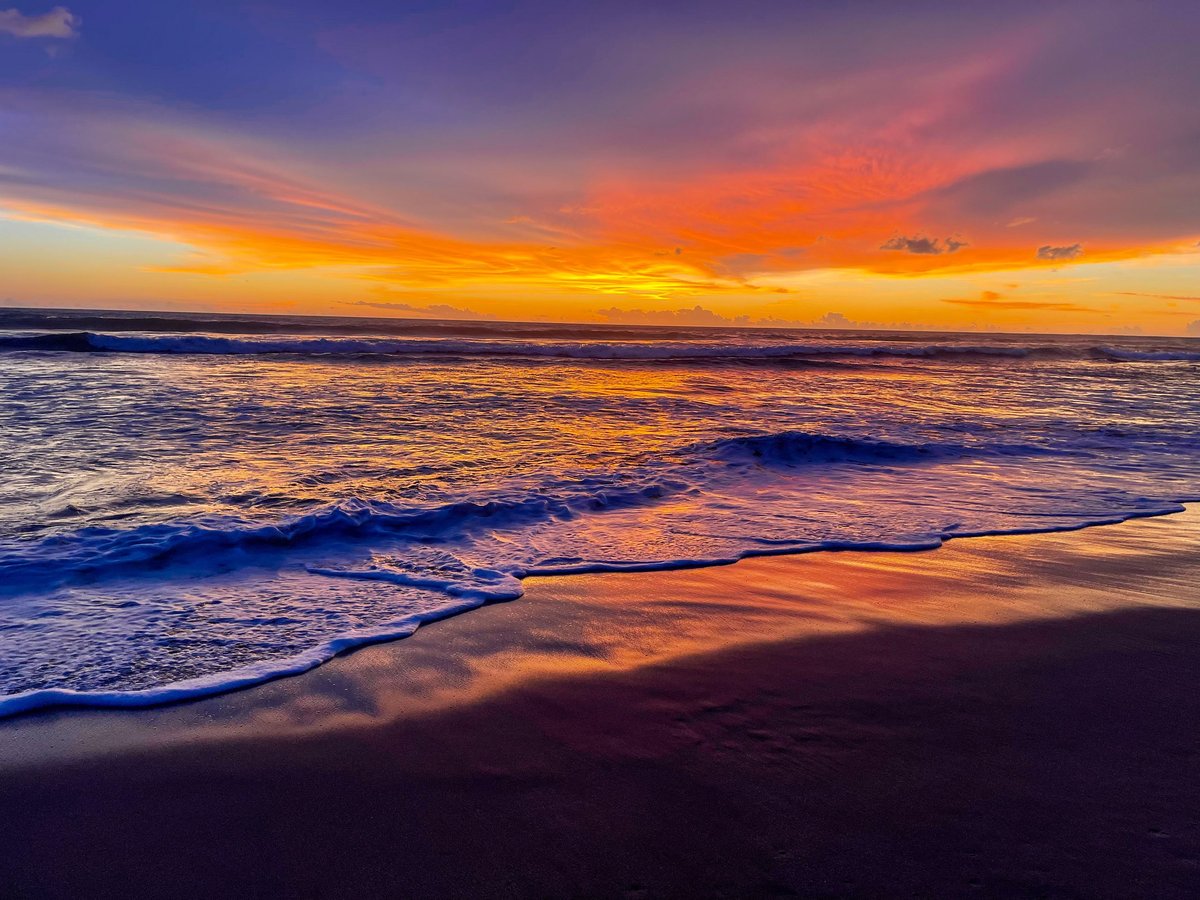 Golden hour sunset over Tamarindo beach with gentle waves and warm orange and purple reflections on the ocean